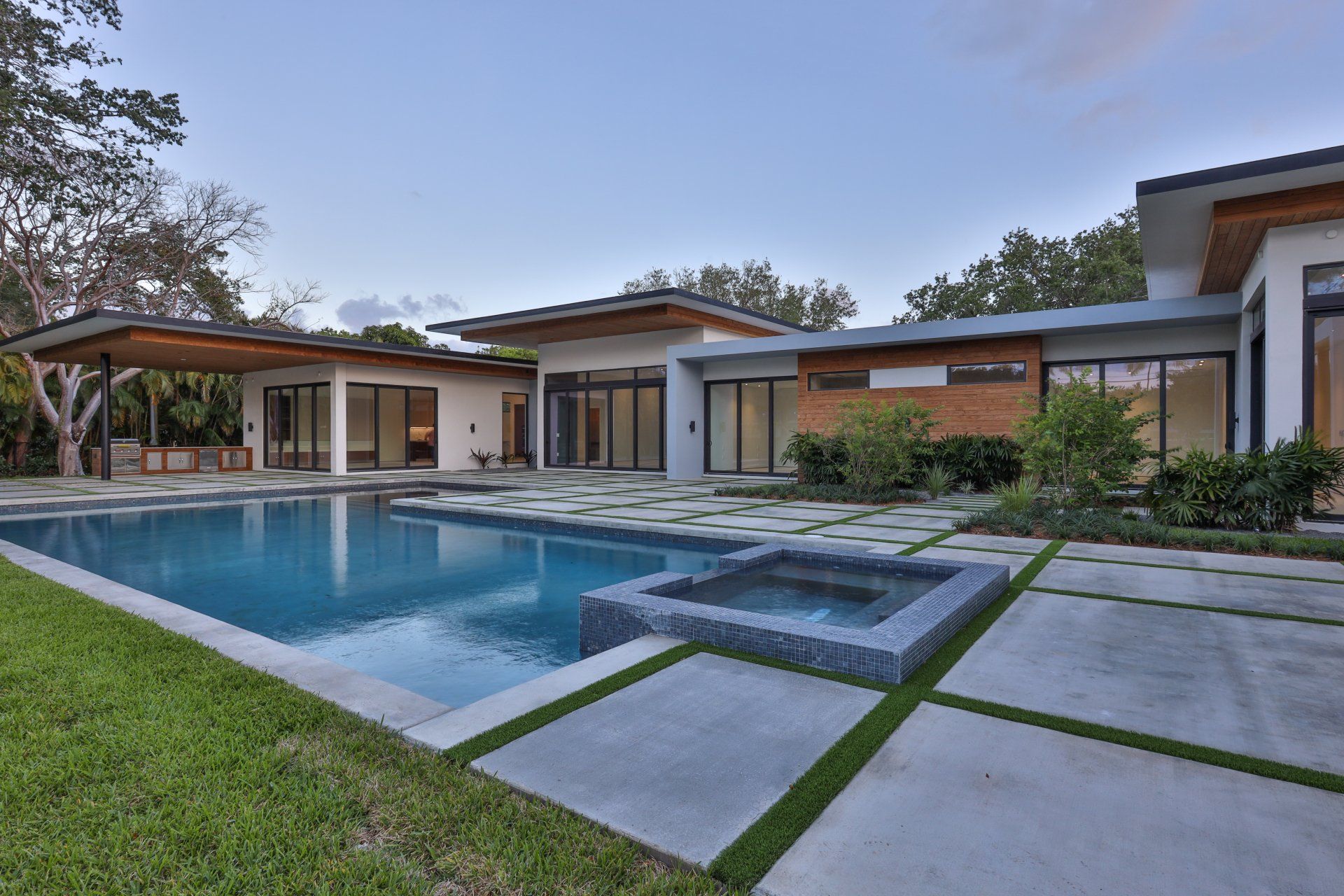 Modern home with pool and spa, concrete patio, and lush green lawn.