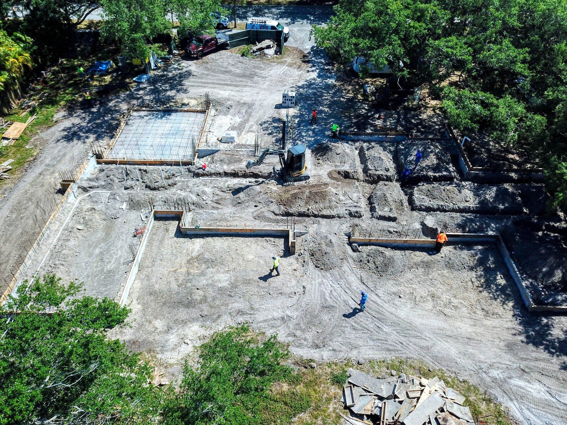 Construction site with exposed foundations and dirt; workers and equipment present.