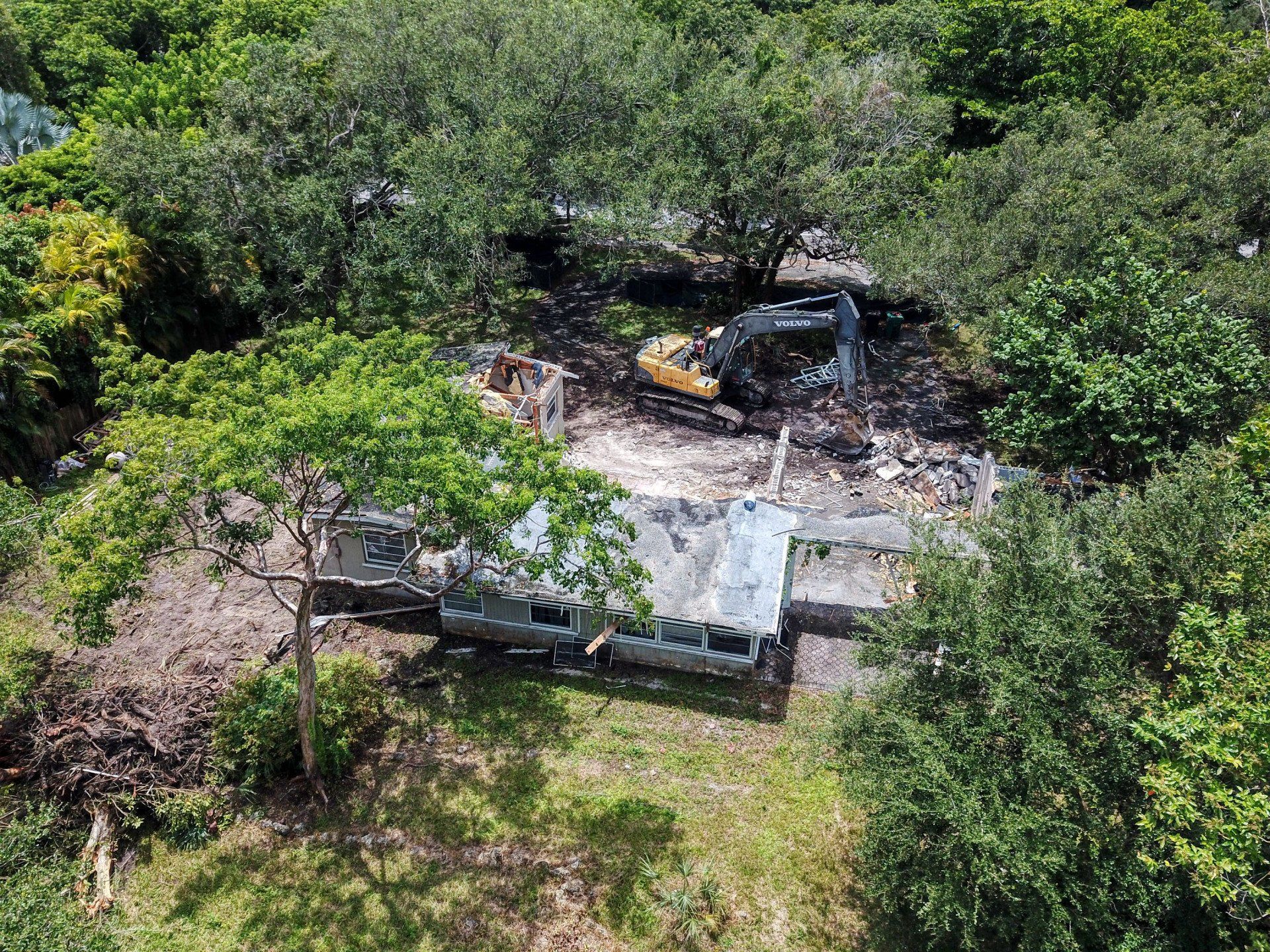 Aerial view of construction site with excavator, surrounded by trees.