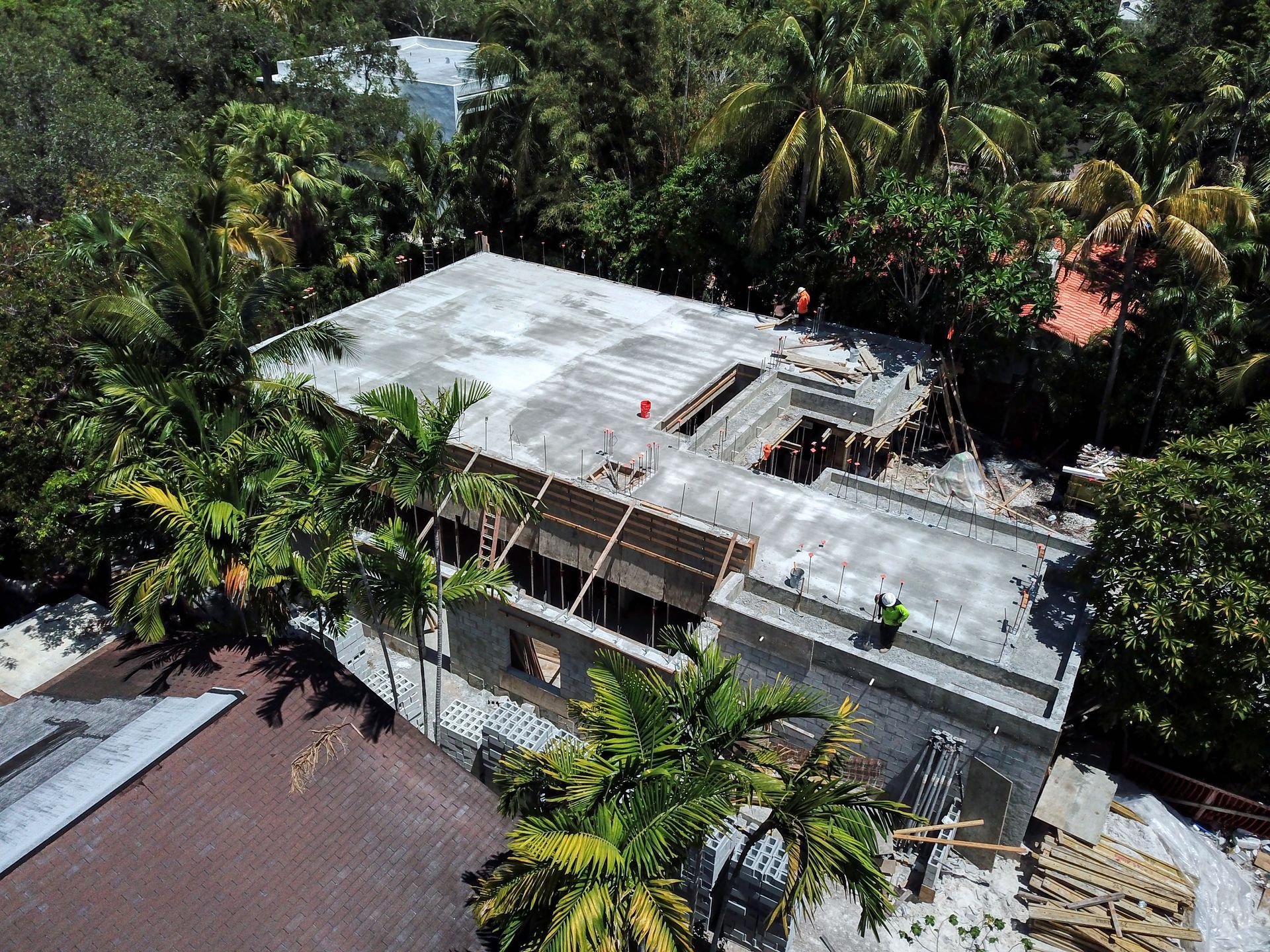 Aerial view of a concrete building under construction, surrounded by lush green trees.