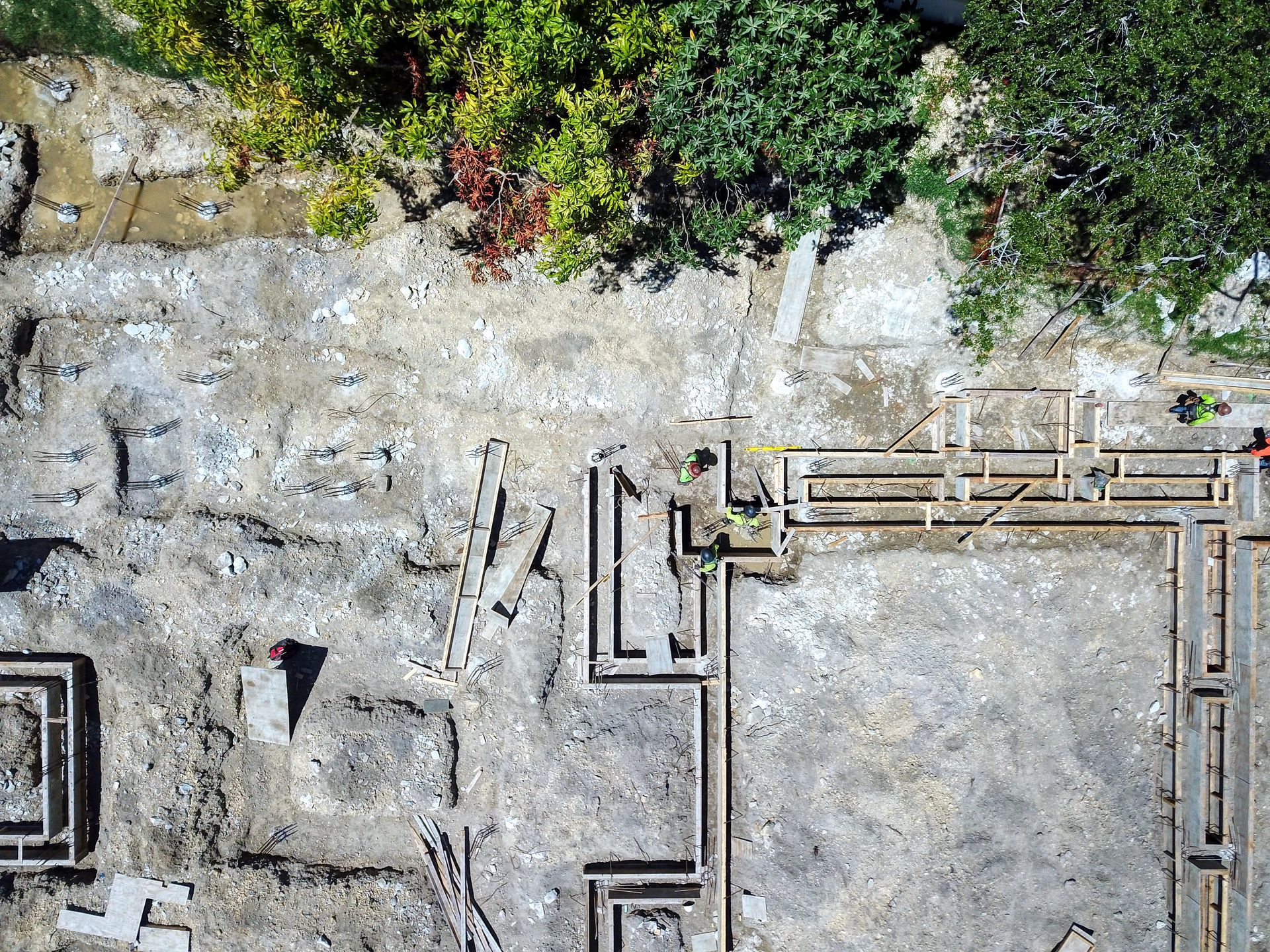 Overhead view of an archaeological excavation site with foundations and some greenery.