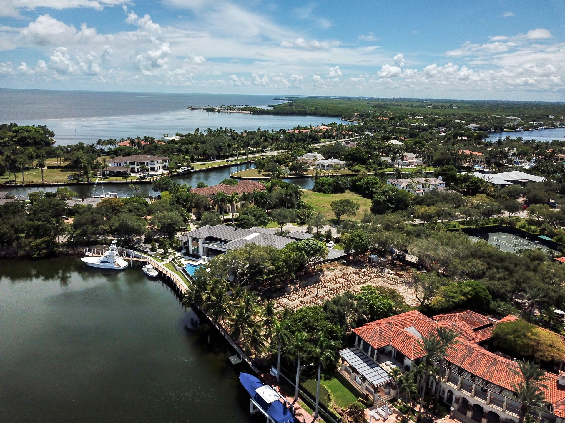 Aerial view of a coastal community with houses, canals, trees, and a body of water under a partly cloudy sky.