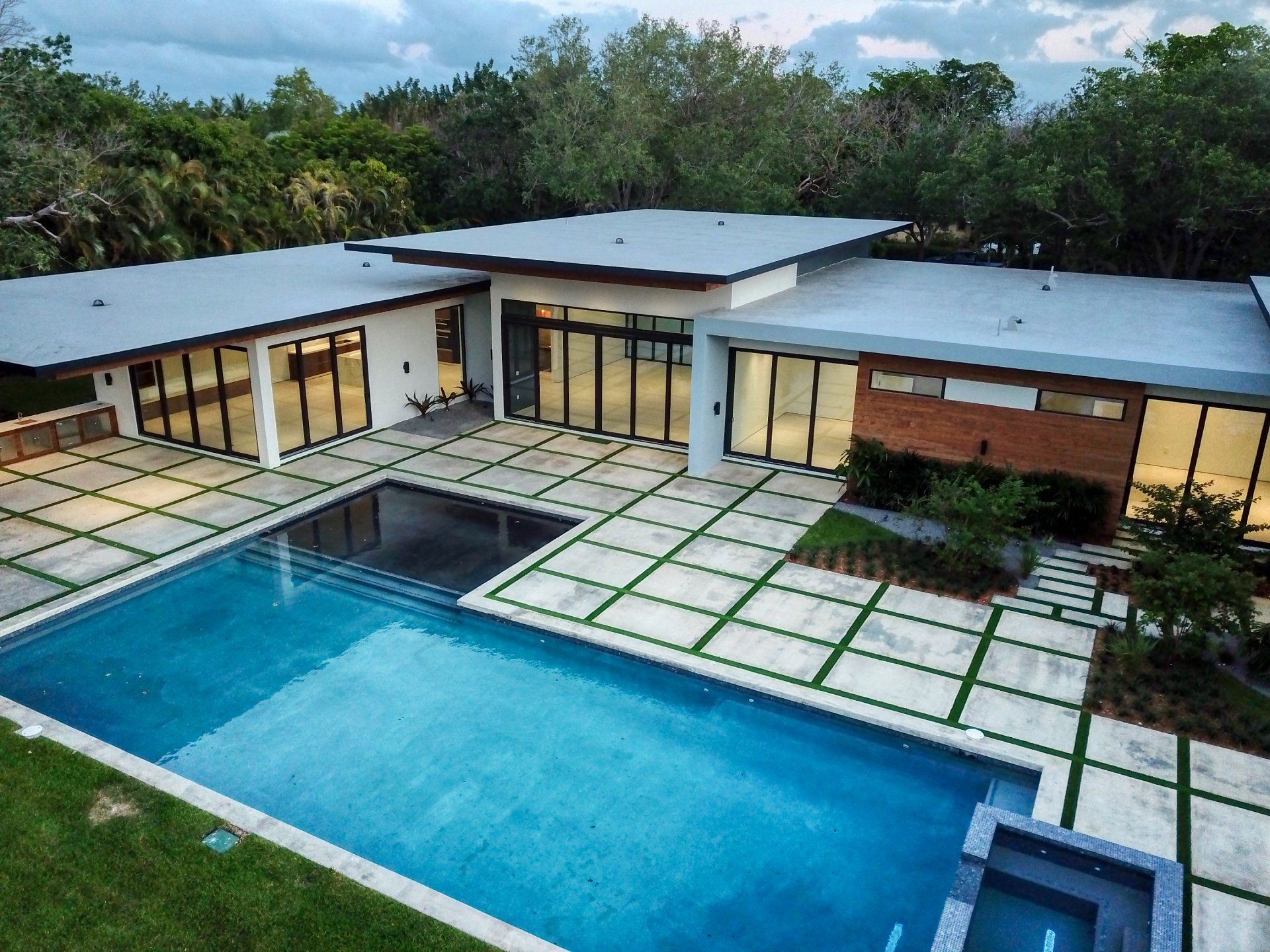 Modern home with pool; glass walls, brick accents, and concrete patio.