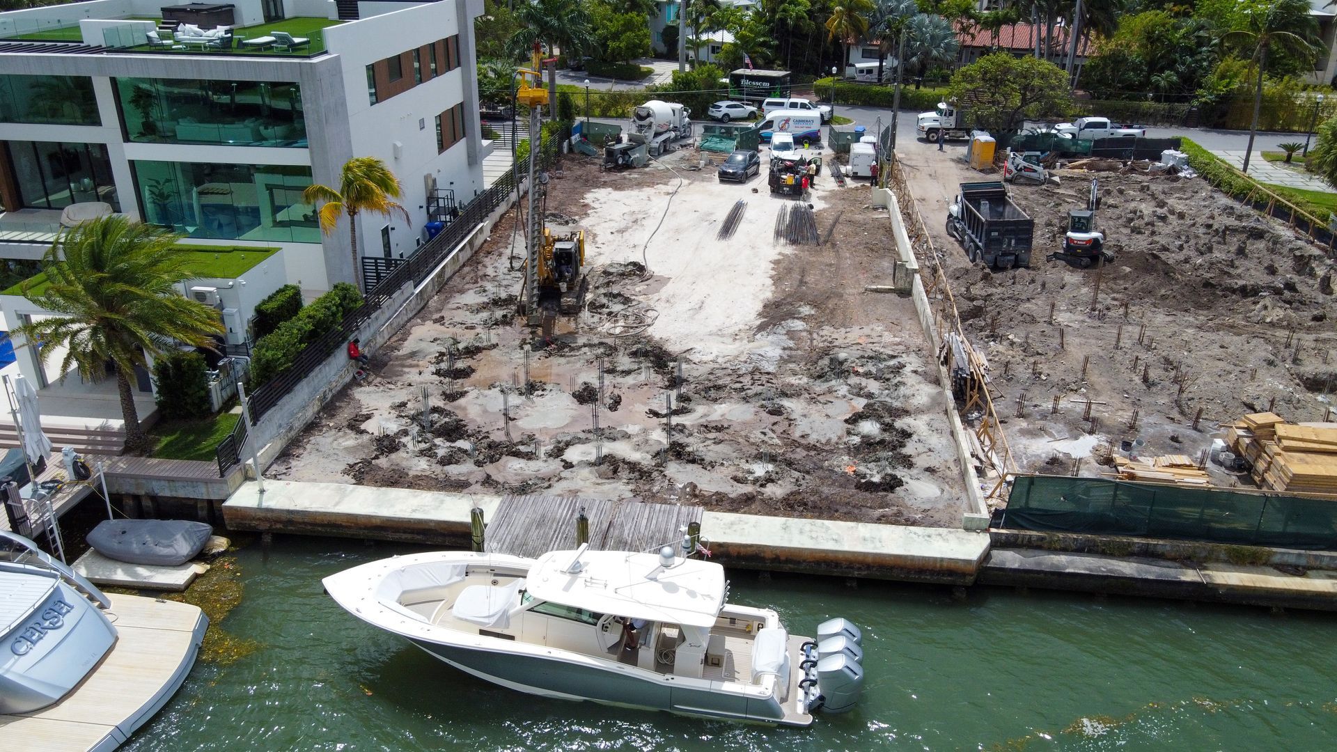 Construction site adjacent to water with heavy machinery, boat, and luxury buildings.
