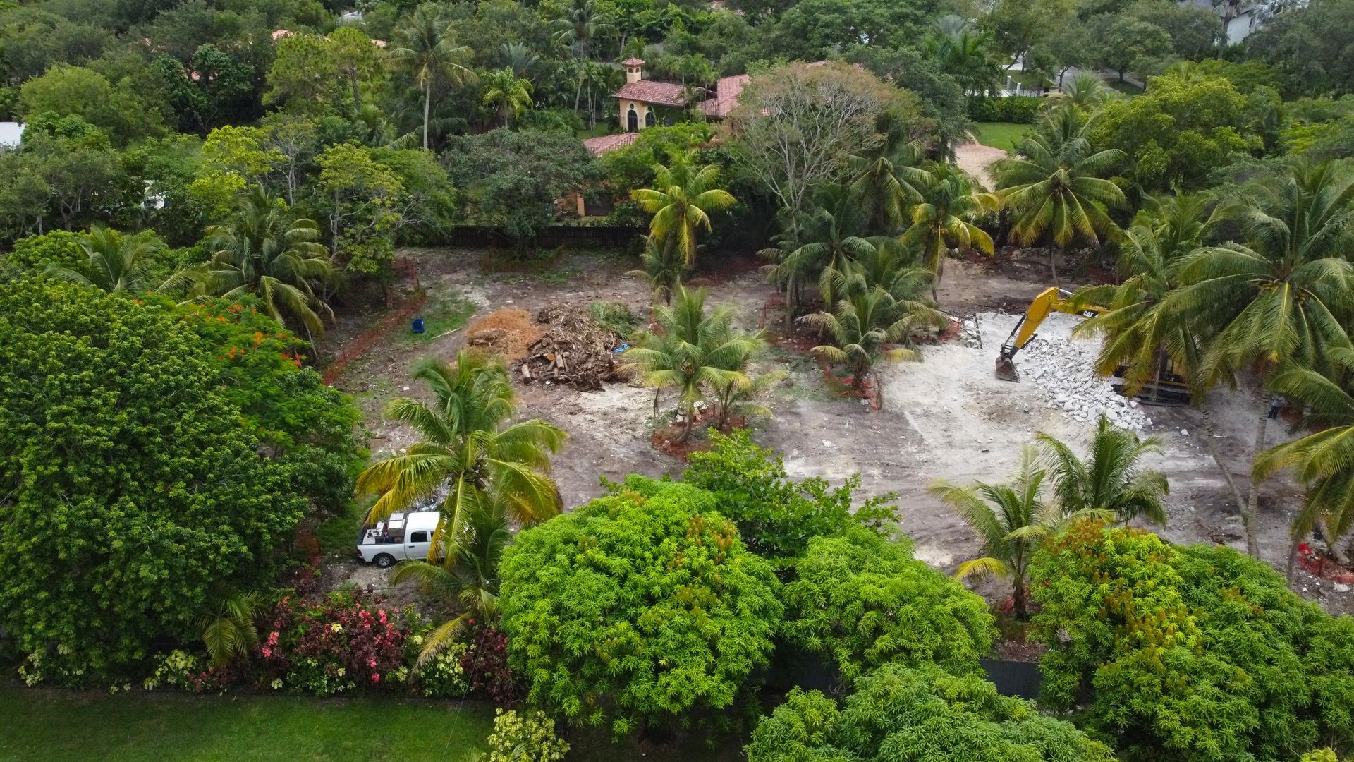 Aerial view of a cleared lot with construction equipment surrounded by lush green trees and foliage.
