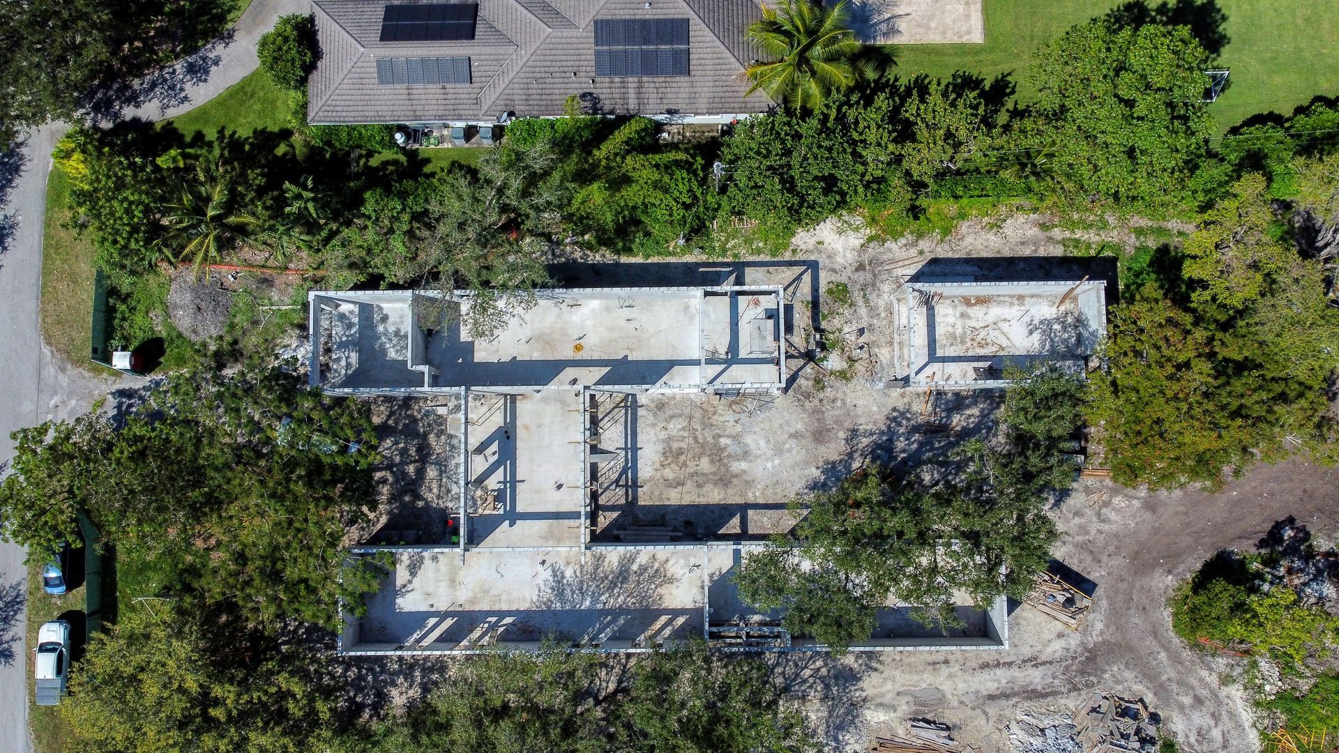 Aerial view of a partially constructed concrete building foundation surrounded by trees and vegetation.