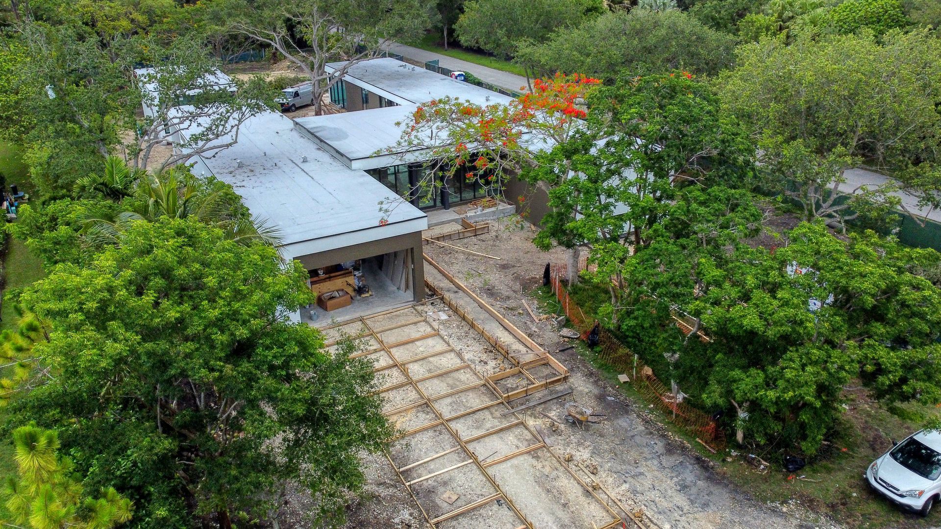 Aerial view of a modern building under construction surrounded by trees and a dirt path.
