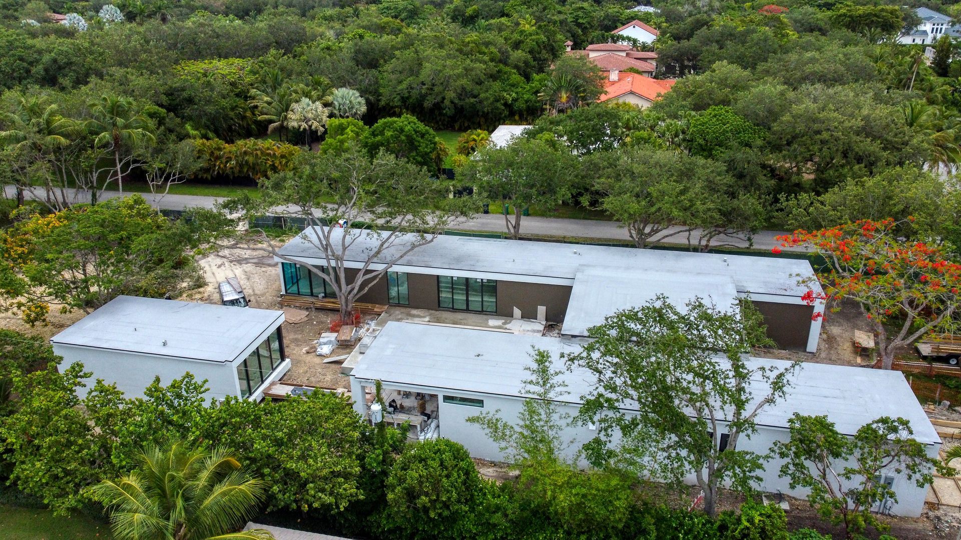 Aerial view of a contemporary house under construction, surrounded by lush green trees and foliage.