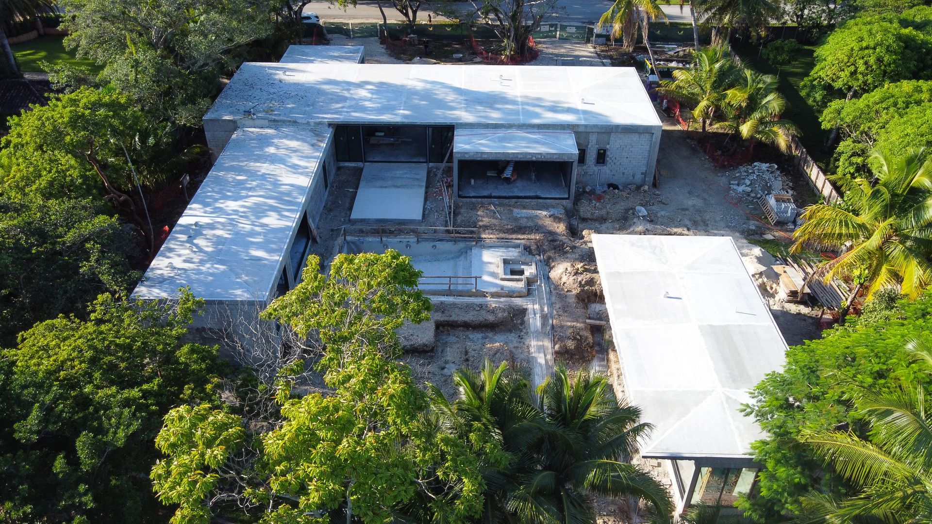 Aerial view of a modern, angular home under construction surrounded by trees and vegetation.