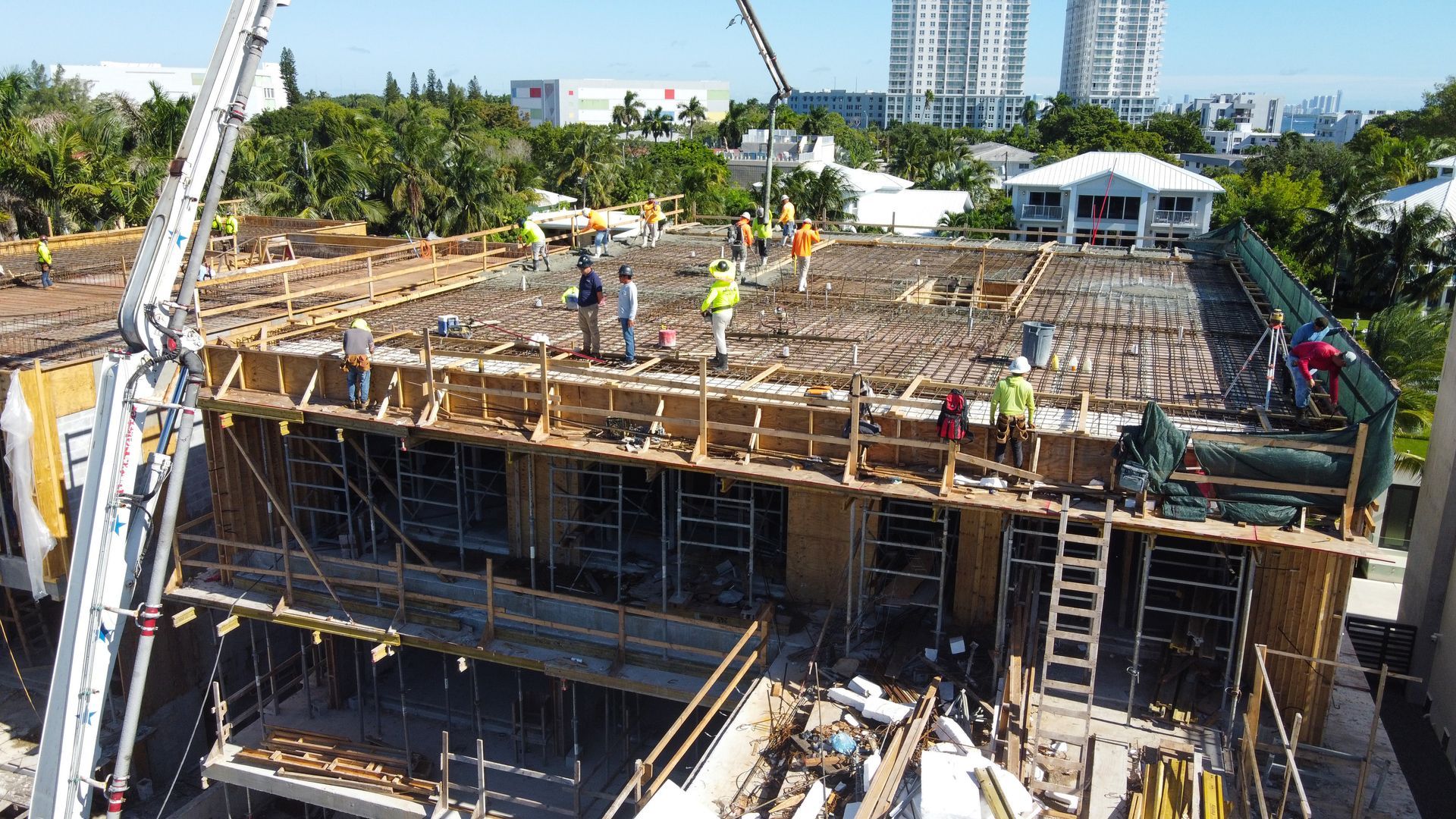 Construction workers pouring concrete on a building rooftop. Crane, wooden frames, and surrounding buildings in view.