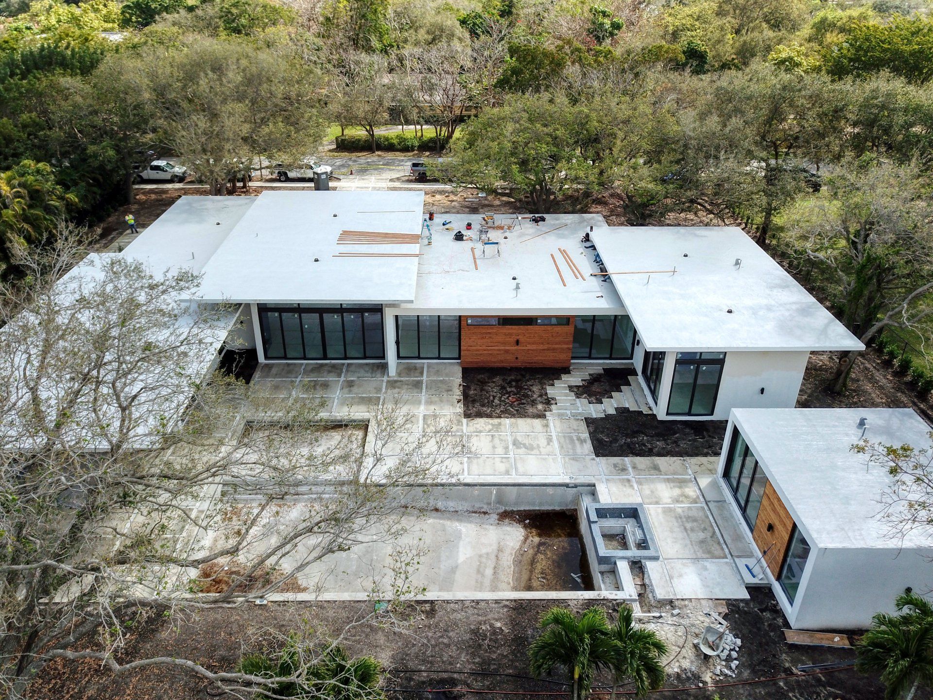 Modern house with flat white roof, glass walls, and wooden accents, surrounded by trees.