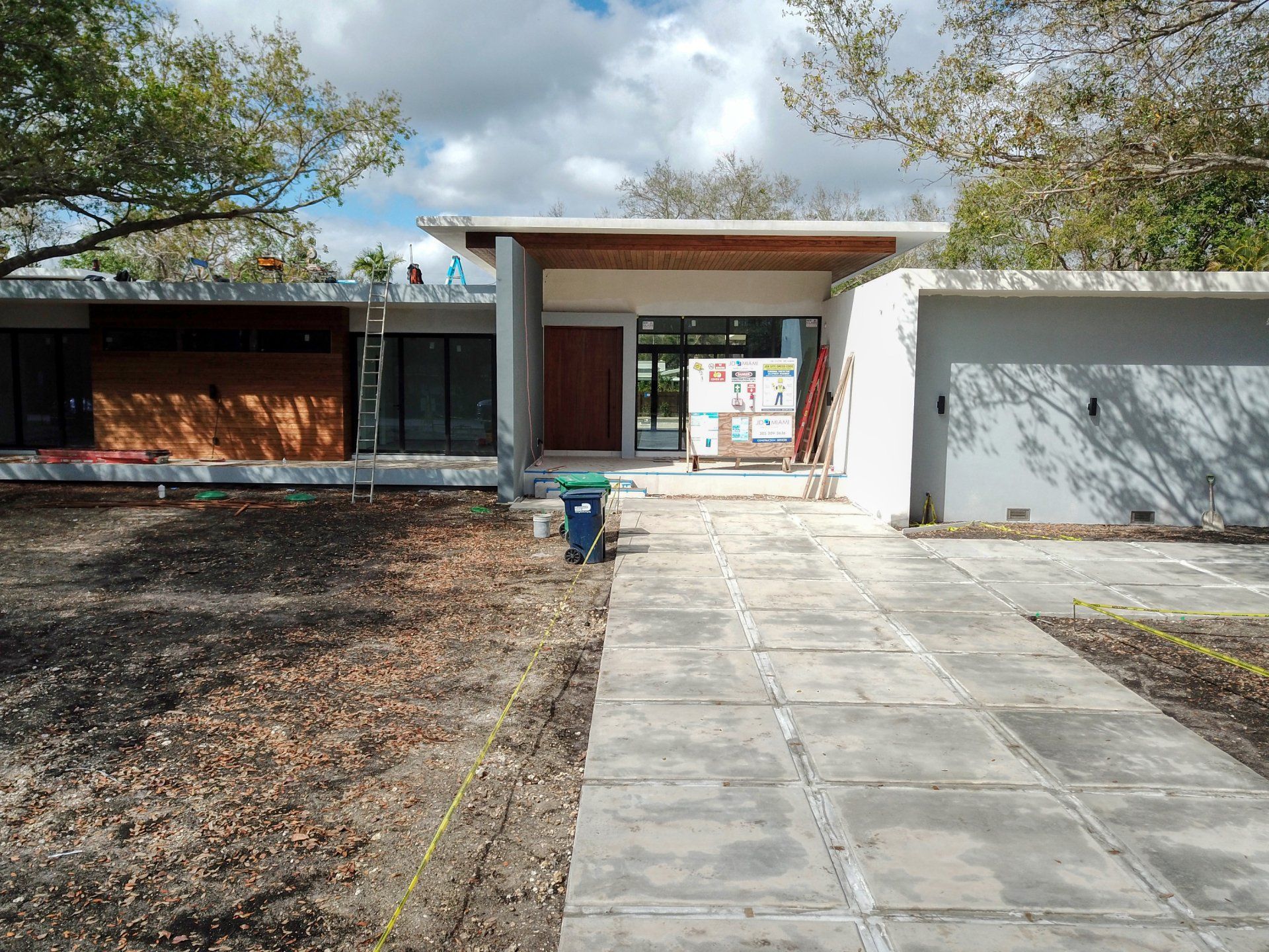 A modern house with a concrete walkway leading to the entrance. Construction materials and tools are visible.