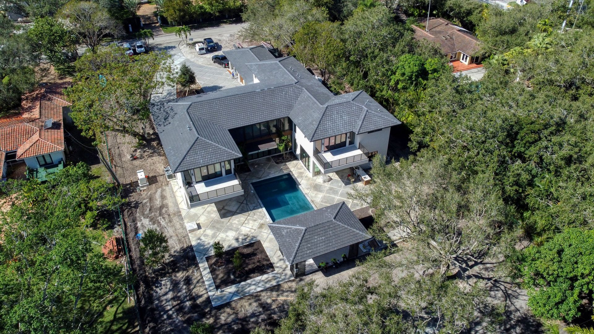 Aerial view of a modern house with a pool, surrounded by trees and a stone patio.