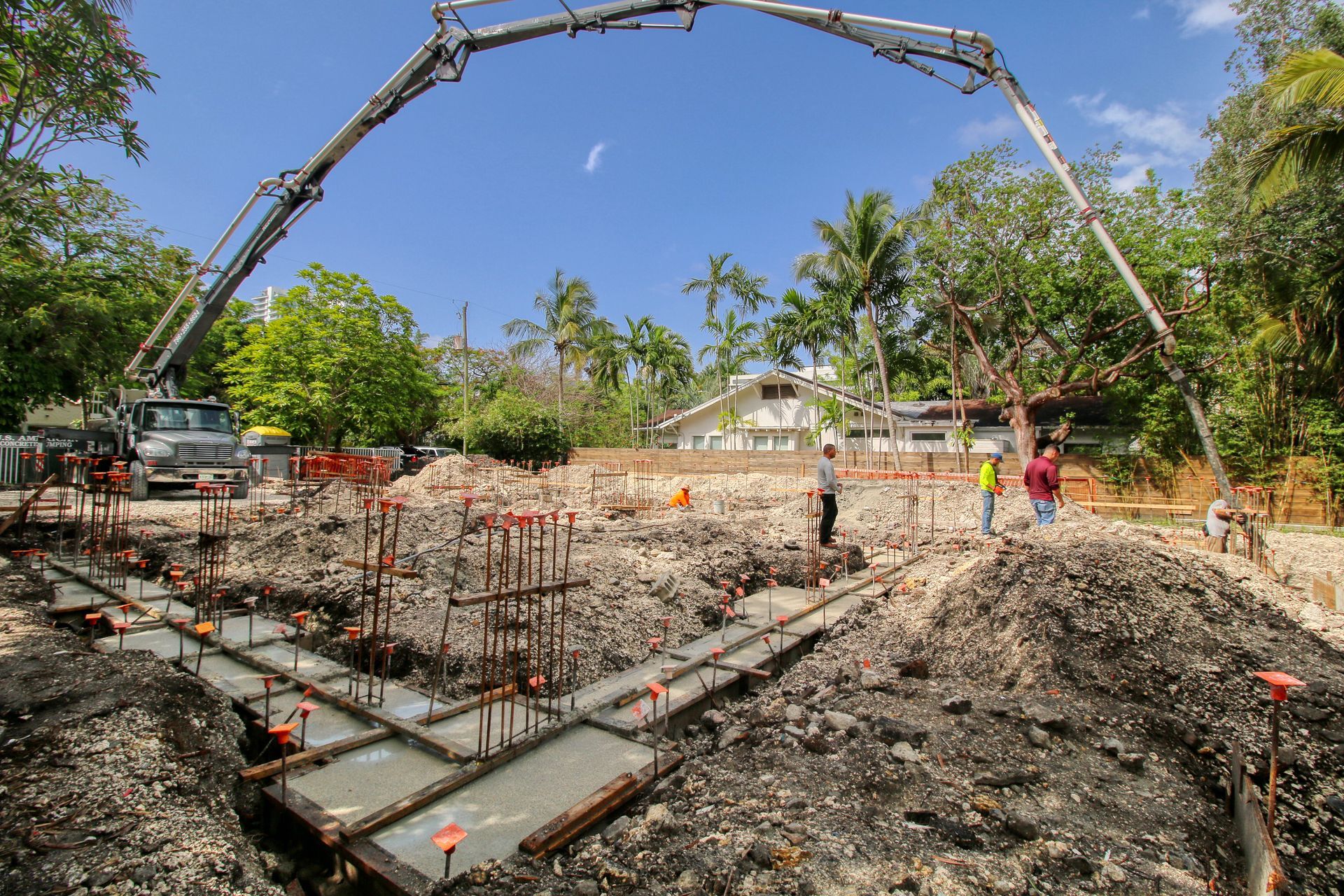 Construction site with concrete pump truck pouring concrete into foundation forms under a blue sky.