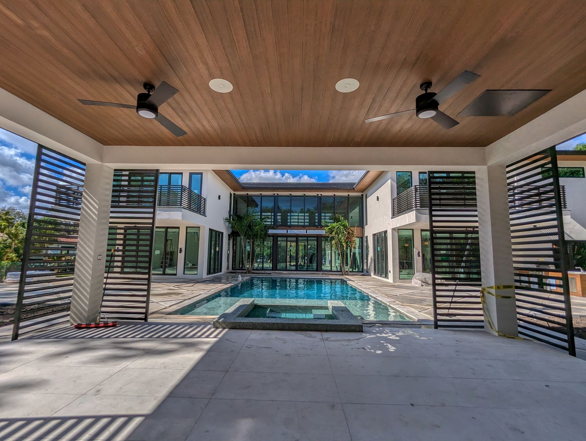 Modern home exterior with pool. Features wood ceiling, open shutters, and glass walls.