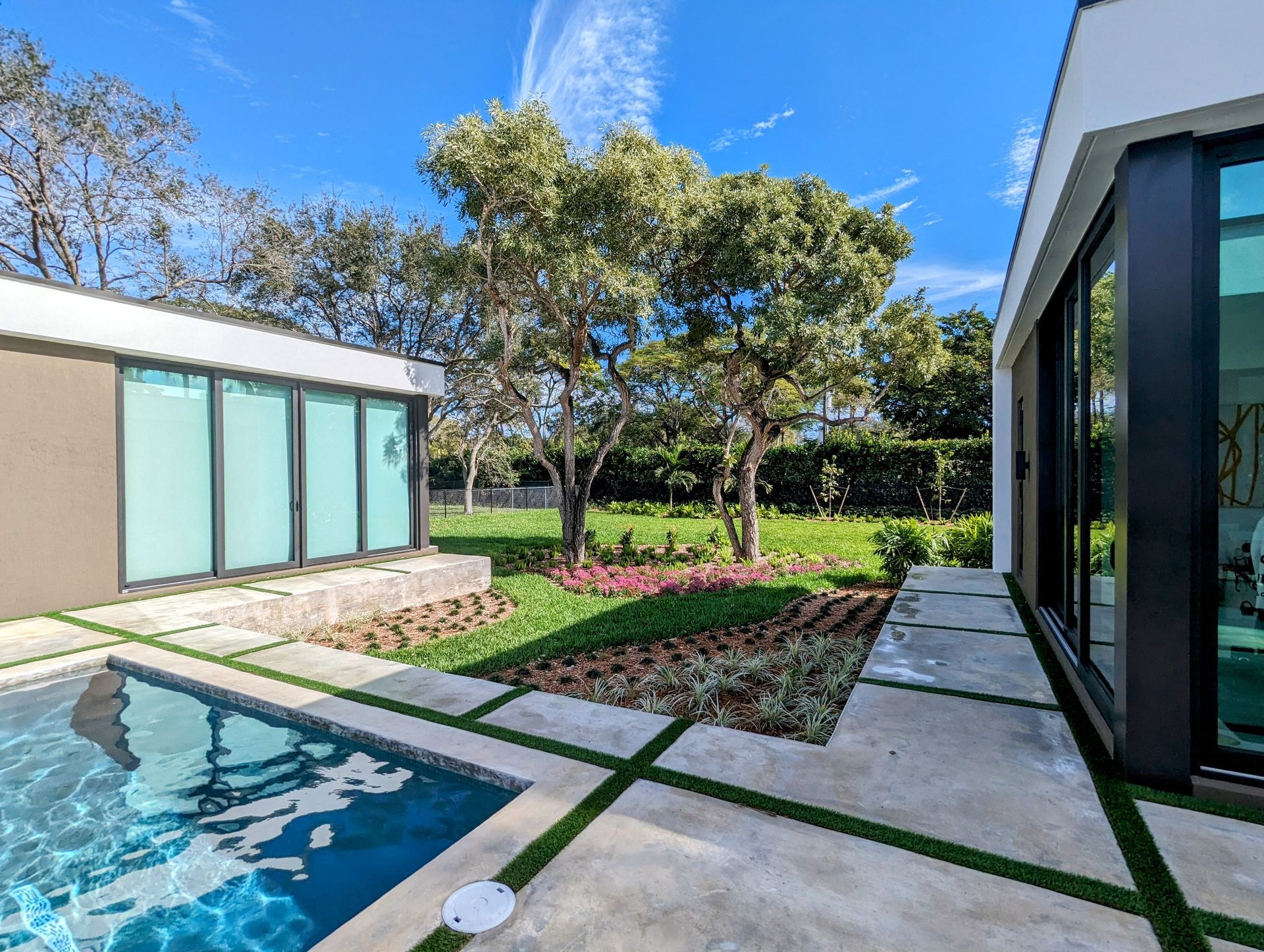 Poolside view of a modern building with large windows and a small garden, under a blue sky.