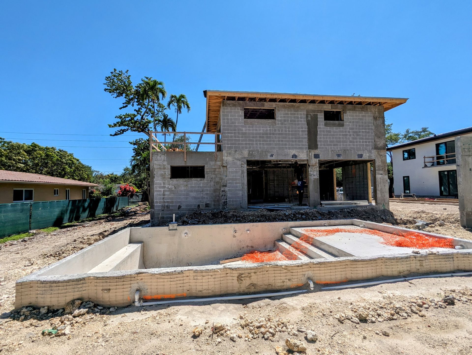 House under construction with a concrete block frame, and a newly built pool. Sunny day.