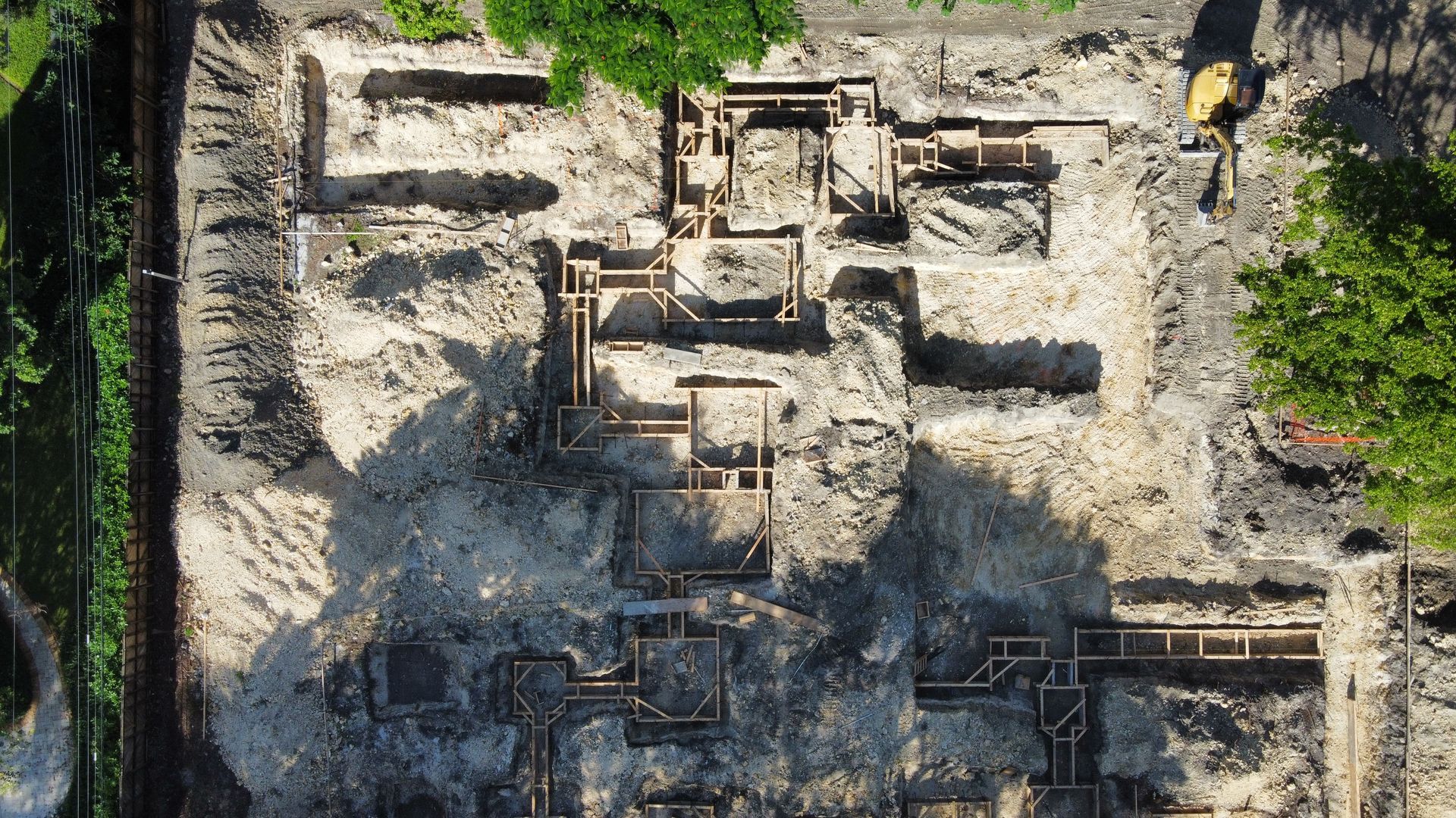 Overhead view of a construction site with excavated foundation outlines, dirt, and some trees.