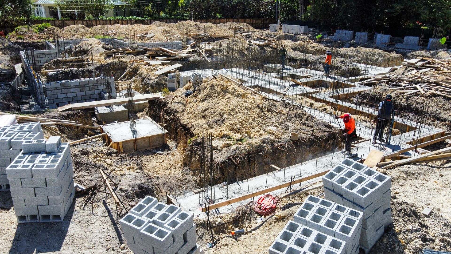 Construction site with workers, exposed foundation, concrete blocks, and rebar.