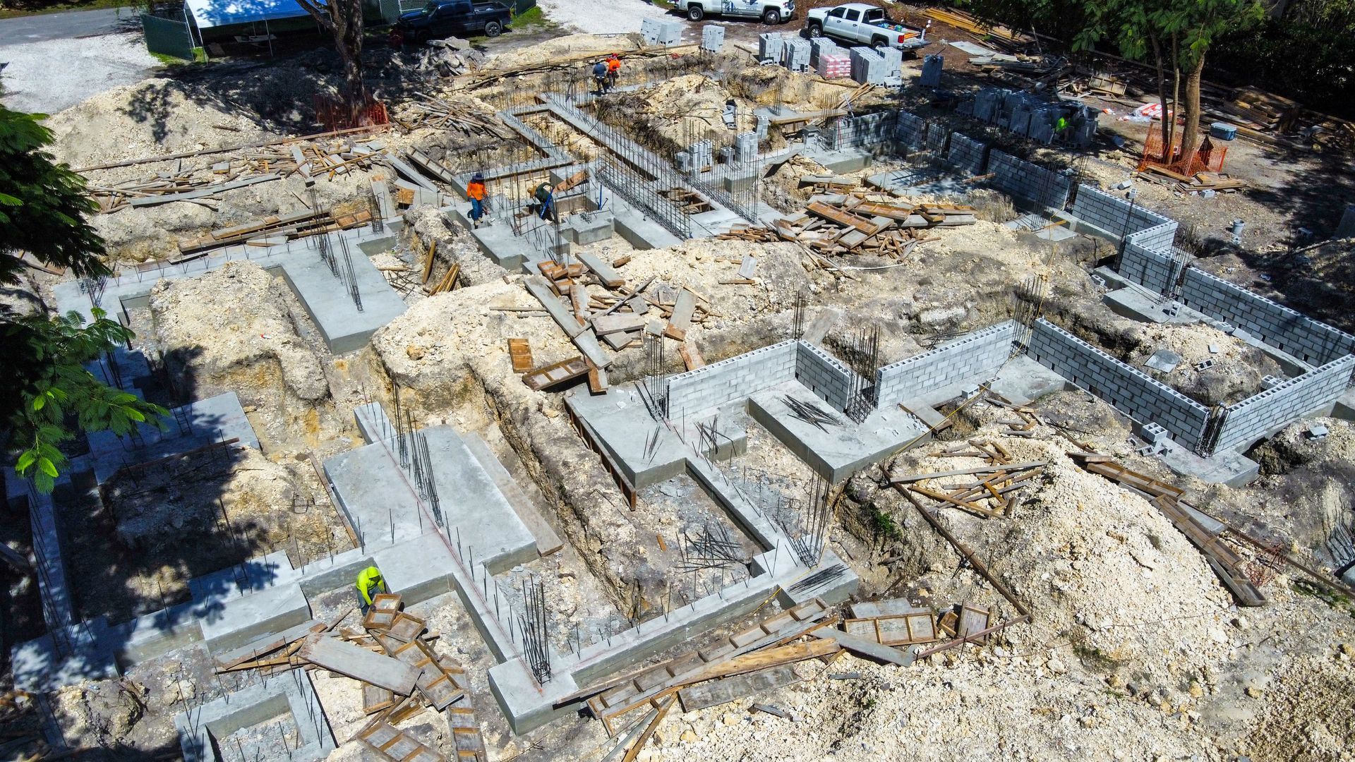 Construction site with foundation walls; workers in orange vests and building materials.