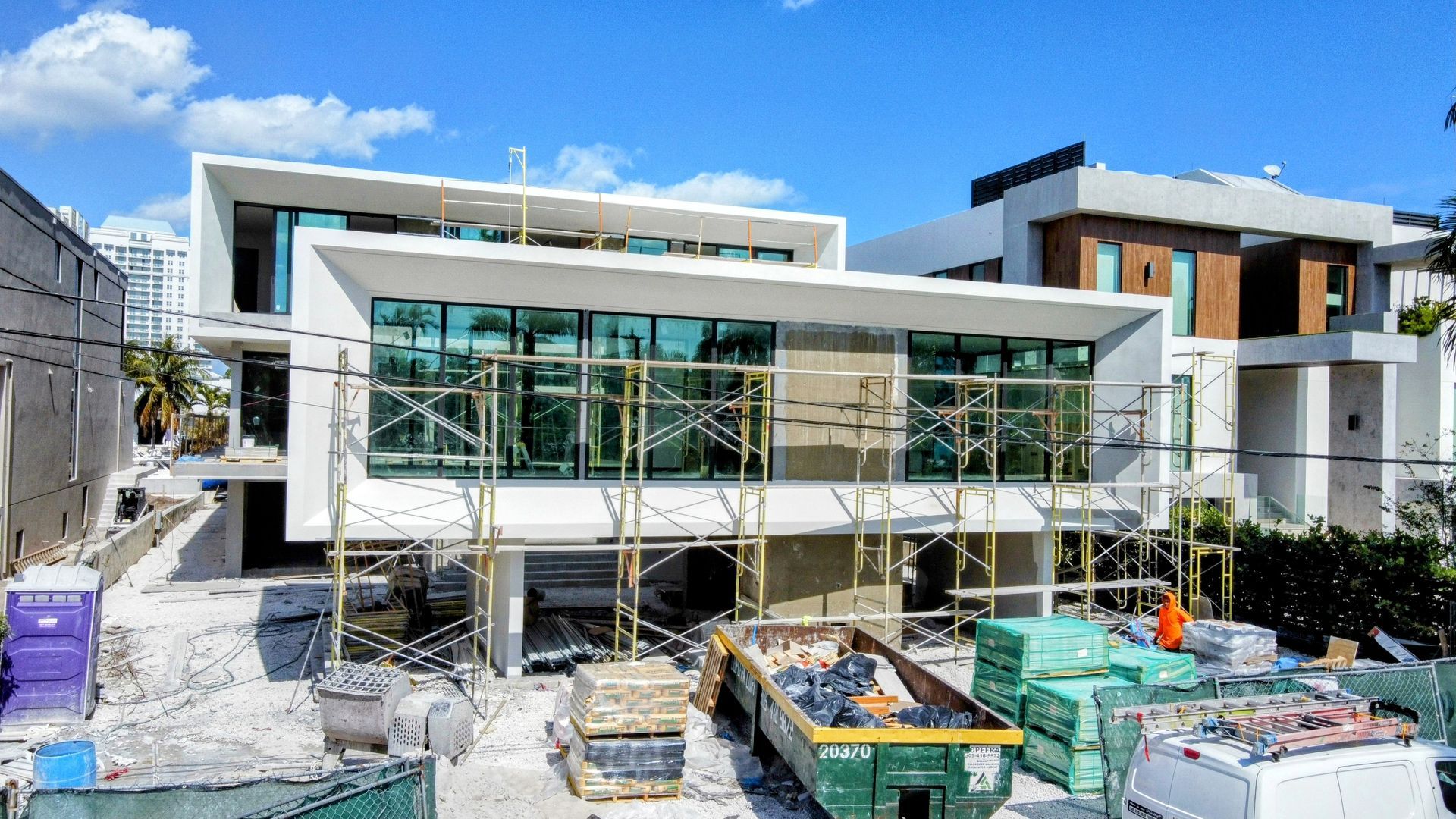 Modern white house under construction with scaffolding, large windows, and construction materials.