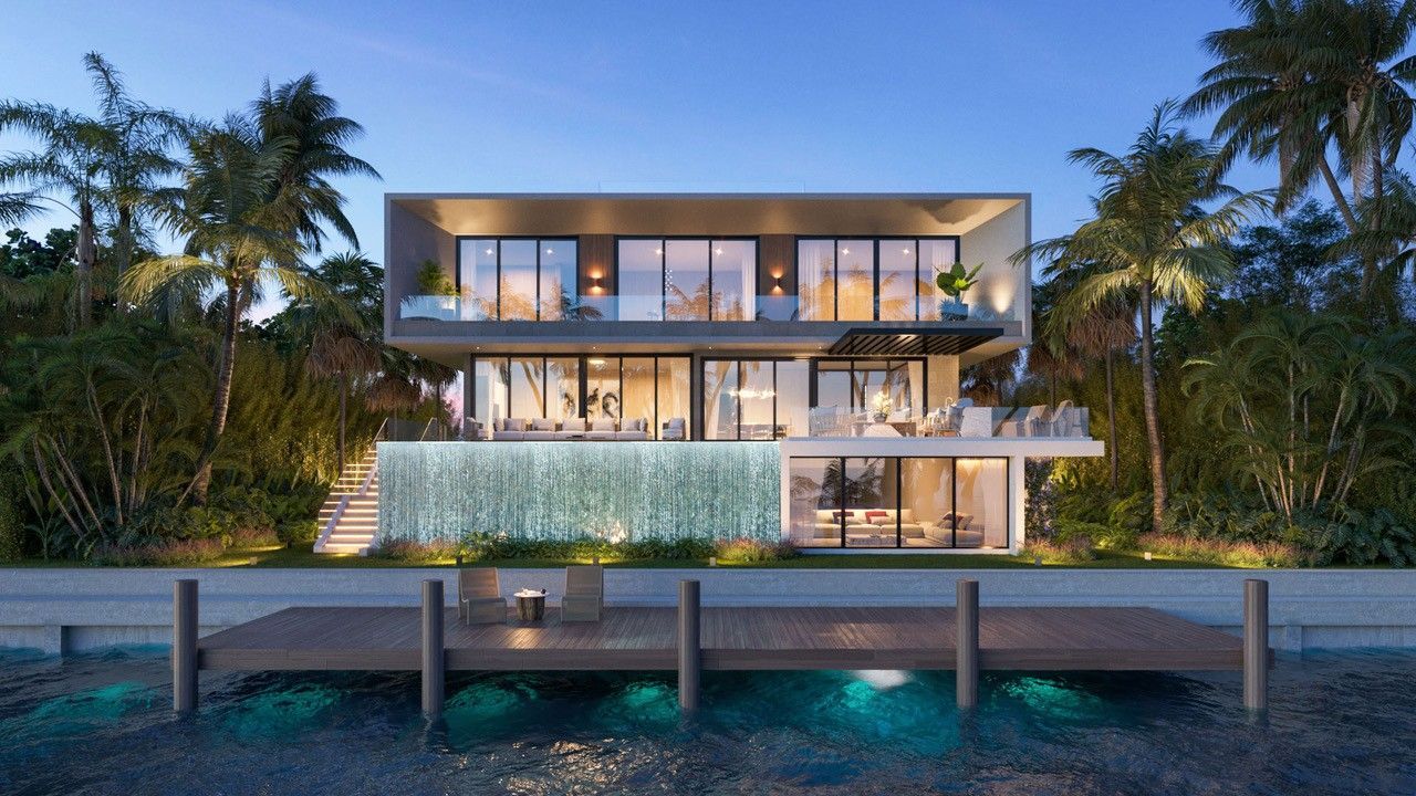 Modern waterfront home at dusk with illuminated waterfall feature and dock.