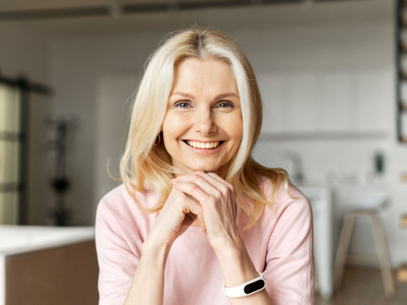 A woman in a pink shirt is smiling with her hands folded