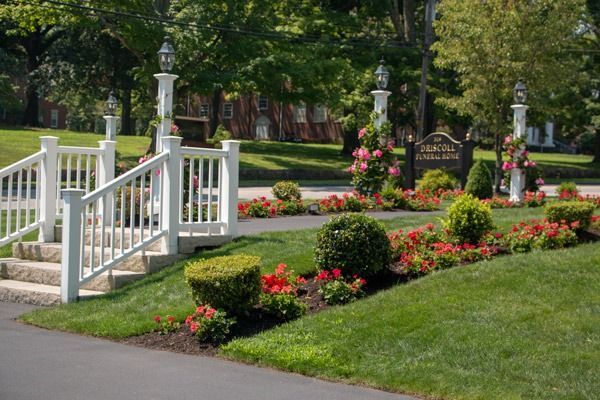 White staircase leads to a sign framed by floral arrangements, surrounded by green grass and red flowers.