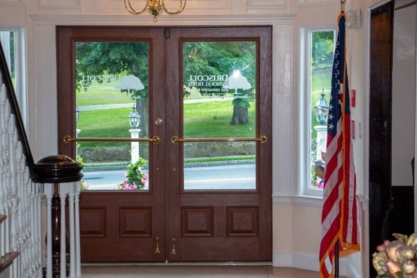 Double wooden doors with glass panels, view of green lawn, American flag to the right.