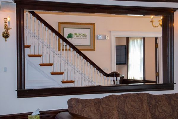 Dark wood-framed mirror reflecting a staircase with white railings, a framed certificate, and a glimpse of another room.