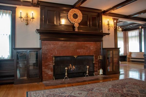 Fireplace with red brick, dark wood, gold sconces, and a decorative wreath.