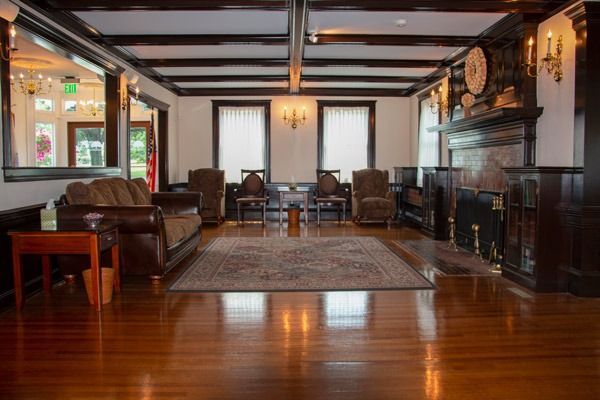 Lounge with wooden floors, dark trim, and fireplace. Furnishings include a sofa, chairs, and a patterned rug.