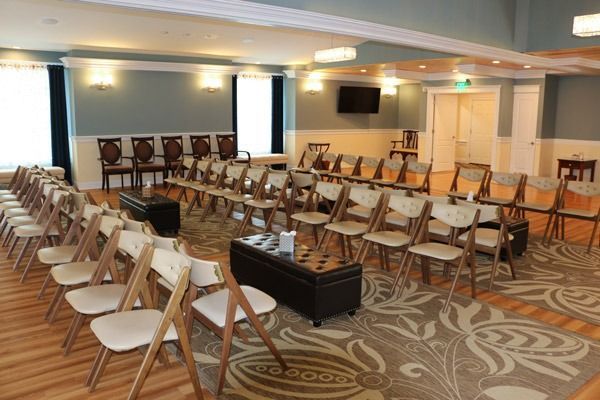 Room set up for an event with rows of chairs facing forward. A TV and closed doors are in the background.