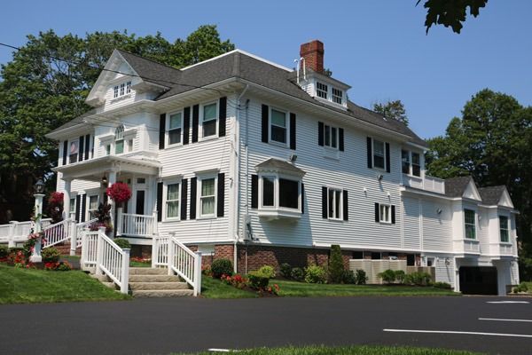 White Victorian house with black shutters, red brick foundation, and small porch.