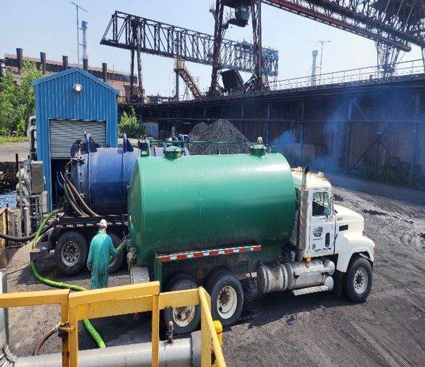 A green vacuum truck is parked in front of a blue building.