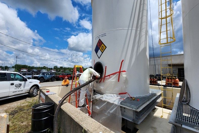 A man is painting a large white tank with a hazard symbol on it.