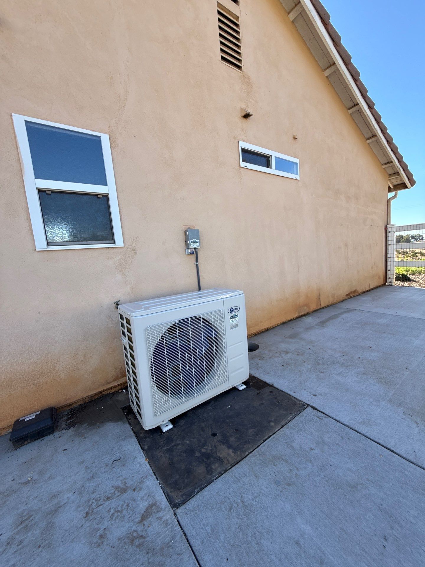 Outdoor wall with a white air-conditioning unit beside a beige house and window