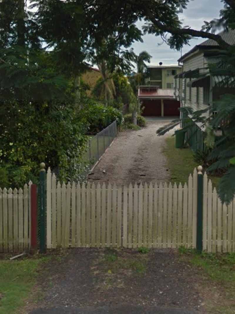 A white picket fence surrounds a driveway leading to a house.