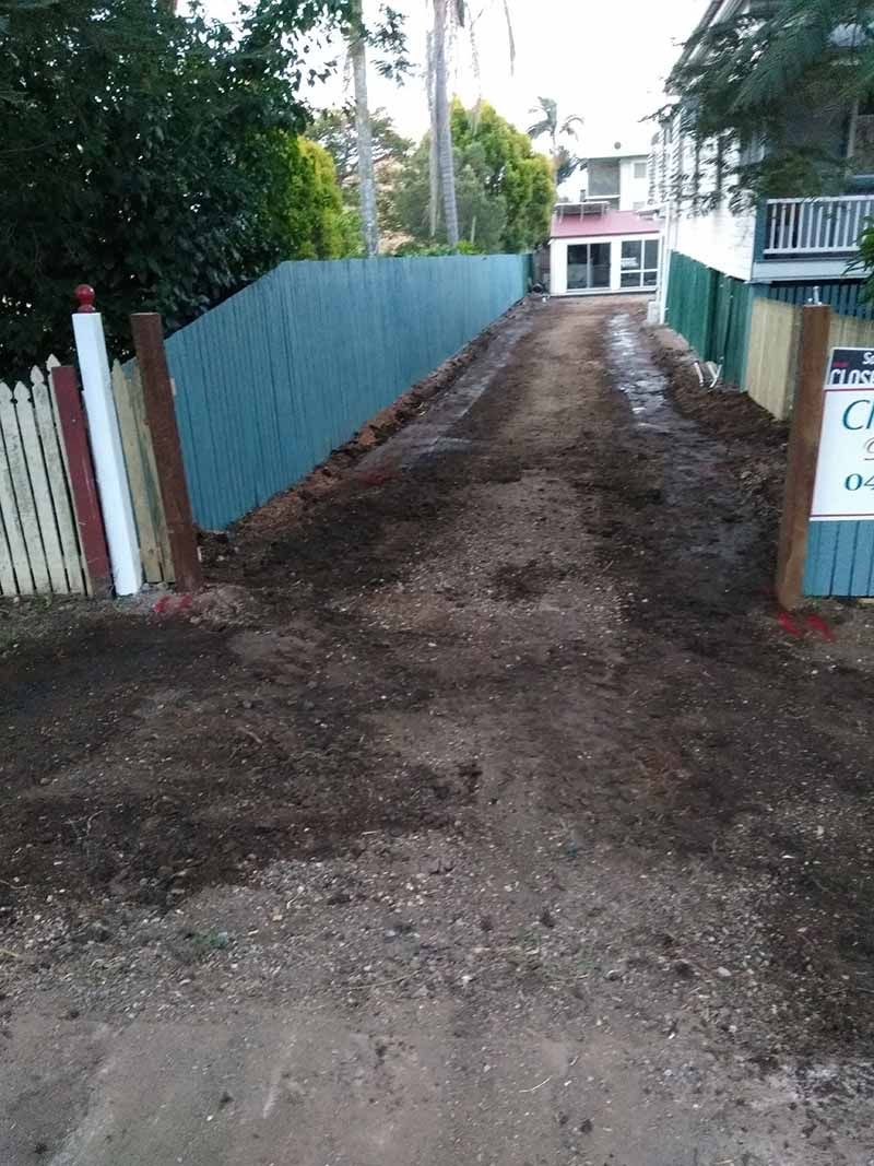 A dirt road leading to a house with a blue fence.