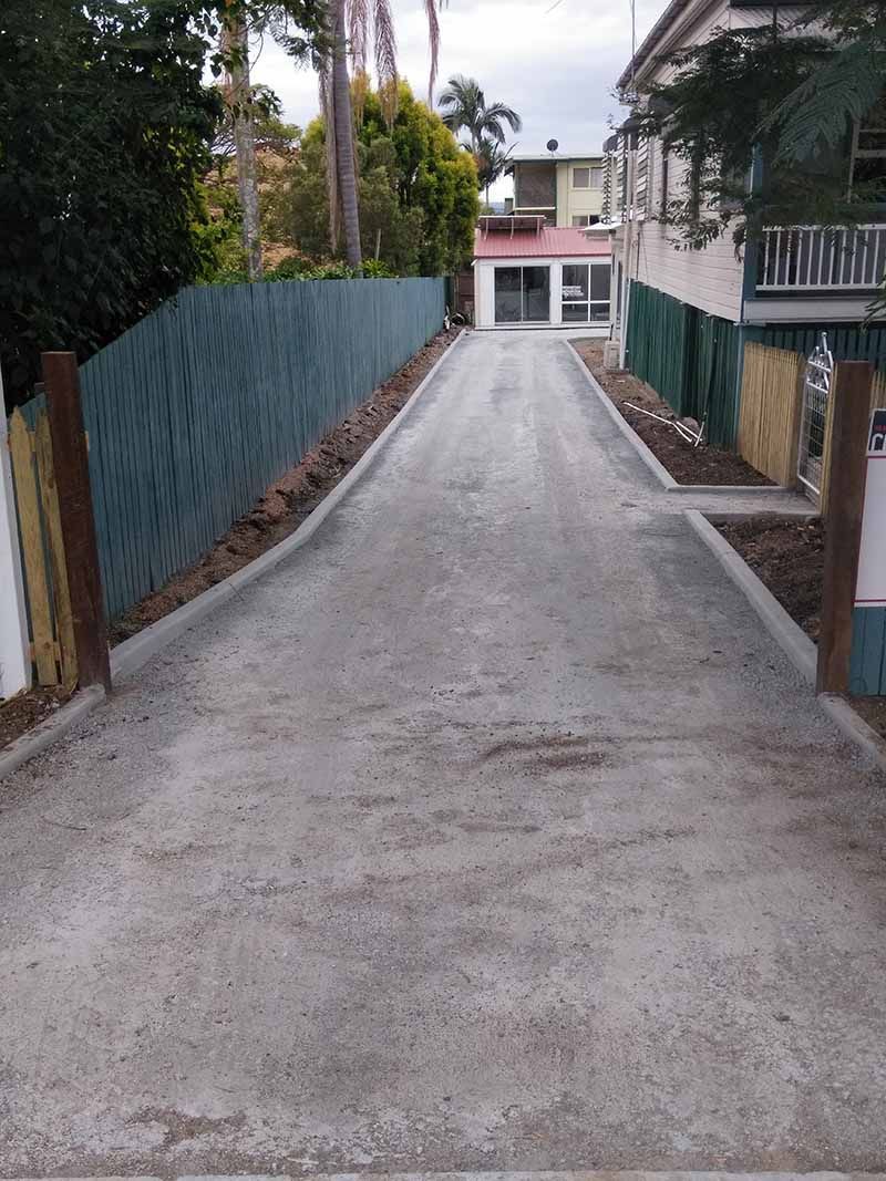 A concrete driveway leading to a house with a blue fence.