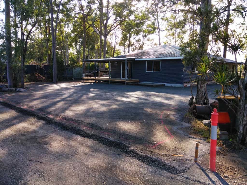 A house is sitting in the middle of a parking lot surrounded by trees.