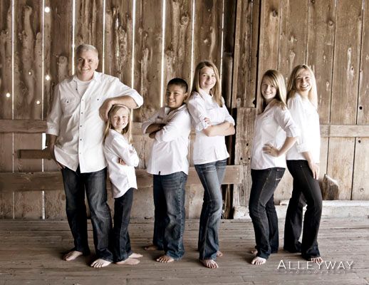 Six people in white shirts and jeans stand together in a rustic wooden barn, posing and smiling.