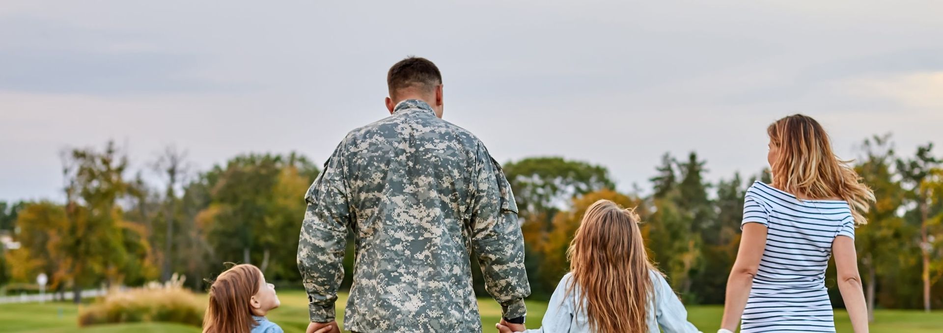 A family of four walking away through a grassy park on a cloudy day