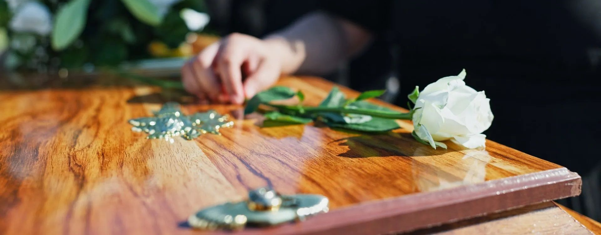 Hands arranging flowers on a wooden table with a white rose bouquet and green foliage
