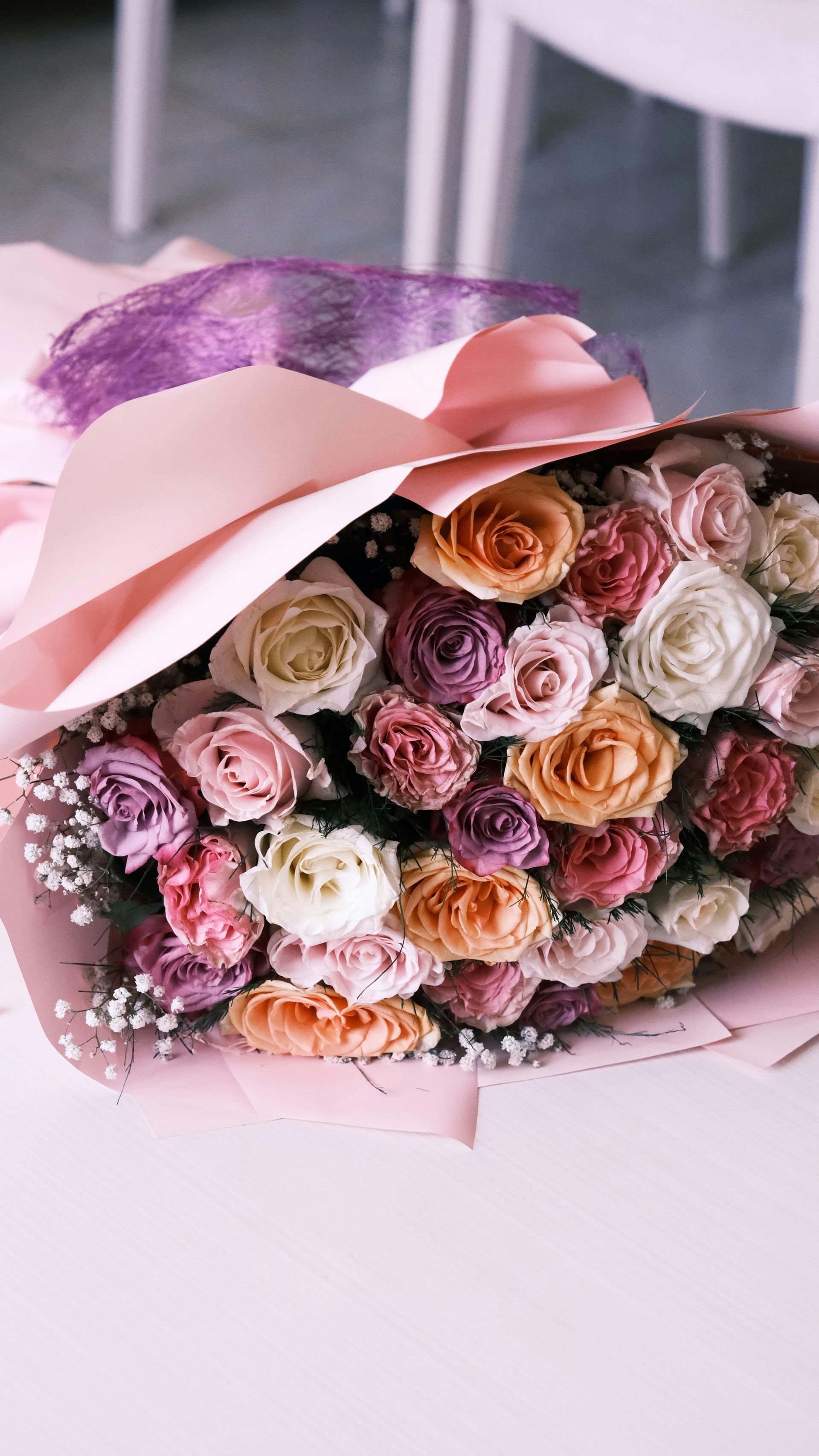Pink and peach roses wrapped in pink paper with a satin ribbon on a white surface