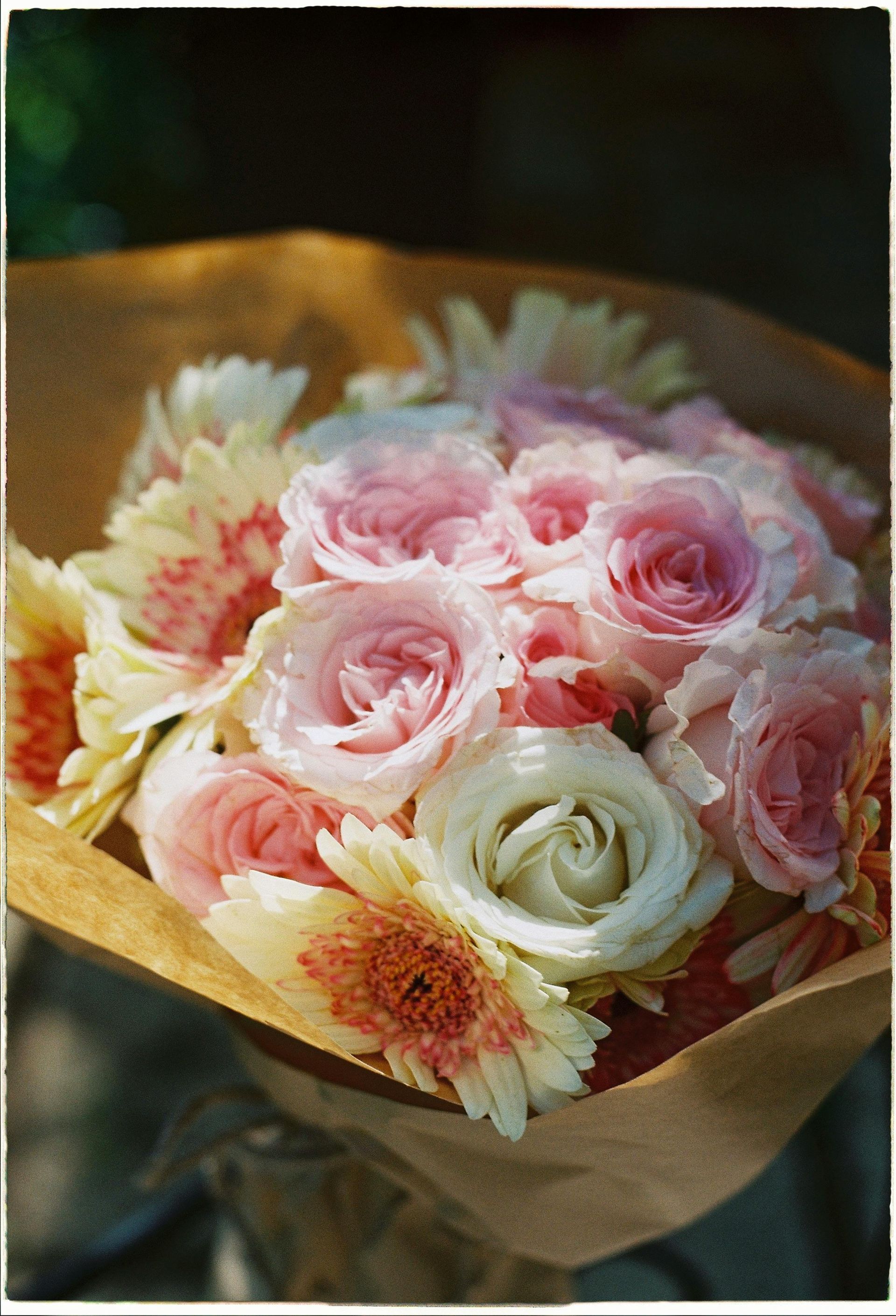 Bouquet of pale pink and white roses with cream flowers wrapped in brown paper