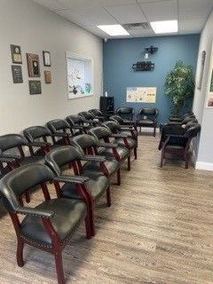 Waiting room with rows of black chairs, blue walls, and a wood floor.