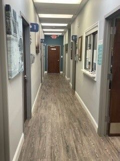 Long office hallway with wood-pattern floor, white walls, and doors on both sides.