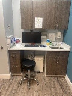 Empty office workstation with computer, stool, and cabinets built into a wood-paneled wall.