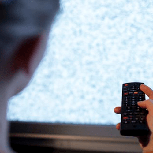 A woman with a tv clicker with white noise on the screen